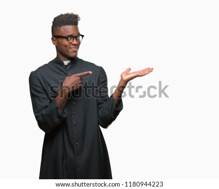Young african american priest man over isolated background amazed and smiling to the camera while presenting with hand and pointing with finger.
