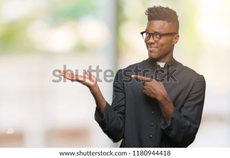 Young african american priest man over isolated background amazed and smiling to the camera while presenting with hand and pointing with finger.