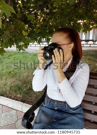 Caucasian business woman optical glasses and white blouse sitting on a bench in the Park and takes a photo on a SLR camera.