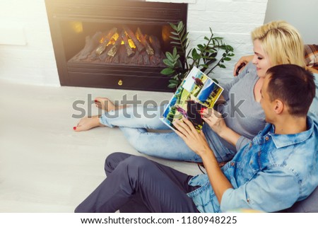 Young Happy Couple Sitting Side By Side On Sofa Looking At Photo Album