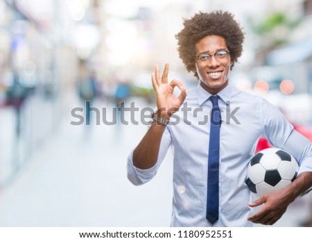 Afro american manager man holding soccer ball over isolated background doing ok sign with fingers, excellent symbol