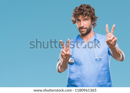 Handsome hispanic surgeon doctor man over isolated background smiling looking to the camera showing fingers doing victory sign. Number two.