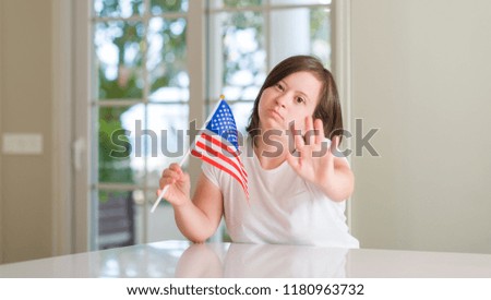 Down syndrome woman at home holding flag of usa with open hand doing stop sign with serious and confident expression, defense gesture