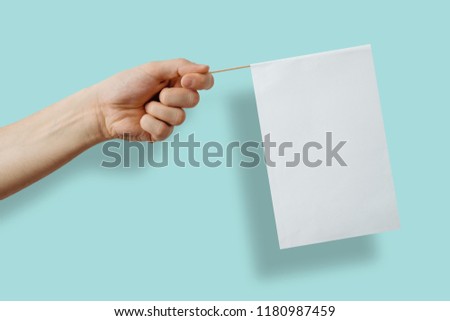 A white, empty flag held in a hand on a green, pastel background. The concept of completing content, manifestations and protesting. Expressing your own views, passing on information.