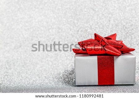 Christmas holiday composition of festive decor gift box with red ribbon on silver glitter bokeh background