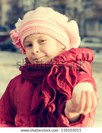 A young girl holds out his hand in a snowball on the playground in a retro style.