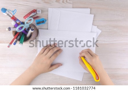 child is going to write an address on an envelope for Santa Claus, a wooden table, writing materials beside