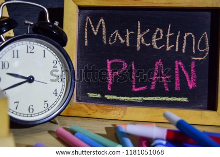 Marketing plan on phrase colorful handwritten on blackboard. Education and business concept. Alarm clock, chalk, books on black background