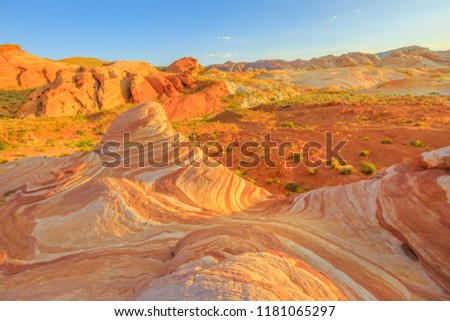 The striped landscape of popular Fire Wave Hike at Valley of Fire State Park in Nevada, United States at sunset colors. Fire Wave is one of the most iconic formations at Valley of Fire. Royalty-Free Stock Photo #1181065297