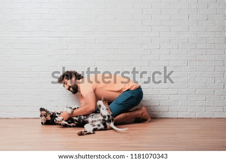 young bearded man with a dalmatian dog against white brick wall background