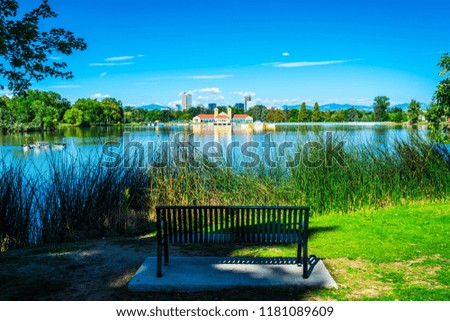 Open Park Bench , a seat to enjoy Green summer morning at City Park in Denver , Colorado , USA with reflection pond and skyline cityscape in the far distance with Rocky Mountains in the background