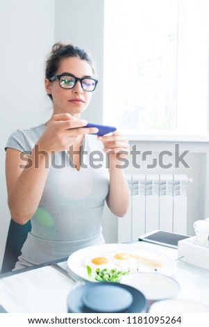 Portrait of Latin-American young woman taking photo of beautiful food via smartphone while enjoying breakfast in cafe, copy space