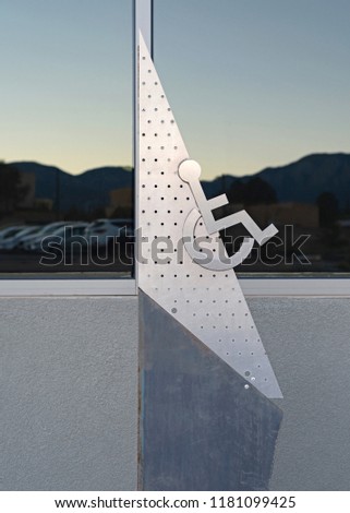 Triangular art deco style handicap parking sign on a grey stand.