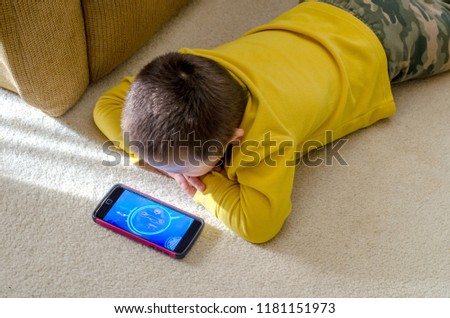 little boy is watching cartoons on moms cell phone on the floor