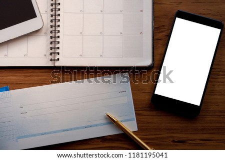 Mock up image of checkbook, pen, year planner and mobile smart phone with blank white screen on wooden table background. Bonus, payment by cheque concept. clipping path.