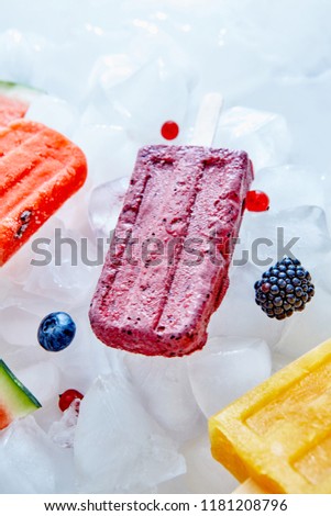 Fruit frozen juice on a stick presented on ice cubes with blueberries, currants and blackberries. Summer dessert. Top view