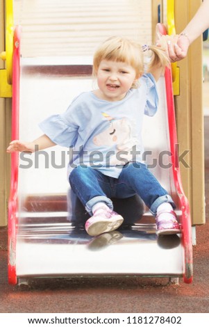 cheerful little blonde girl with two tails playing on the playground in summer sunny weather