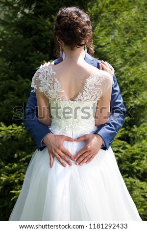 Wedding picture with married couple where groom is hilding hands in shape of heart on back of bride.