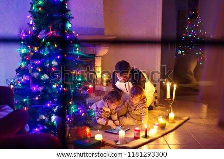 Father and his two little children sitting by fireplace chimney on Christmas Eve time.
