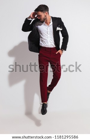 stylish casual man jumping with a hand in pocket and looking down to side near a white wall, full length picture