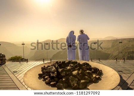 Two mans dressing with arab white clothes in a hotel in Oman. Orange predominance in the picture, feeling of desert, dry place, no clouds