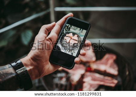 Man taking a photo of beef steaks on his smartphone. Grill and BBQ or barbecue season concept