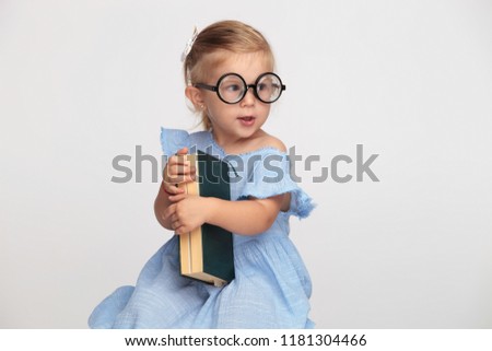 cool nerdy little girl holding her book and waits for the school to start on grey background