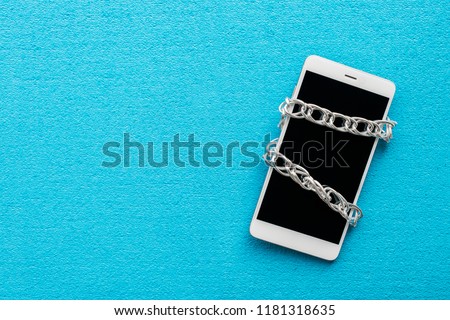 White smartphone with metal chain on blue background. Digital detox, dependency on tech, no gadget and devices concept Royalty-Free Stock Photo #1181318635