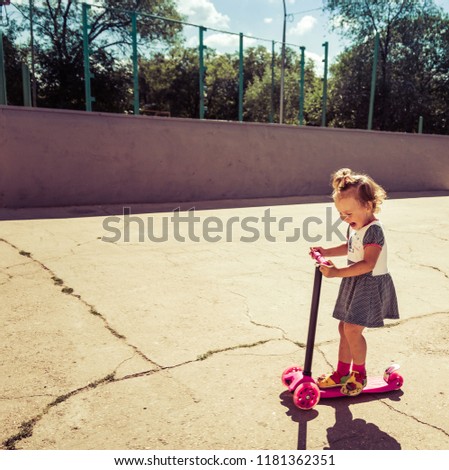 Cute child skilfully skates on a pink two-wheeled scooter on a summer sunny day