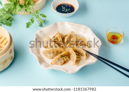 Gyoza dumplings with duck cooked in bamboo steamer served on a plate with soy sauce, sesame seeds and cilantro. Top view, blue background