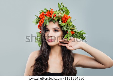 Beautiful woman with healthy curly hair and natural makeup wearing in red berries and green leaves wreath