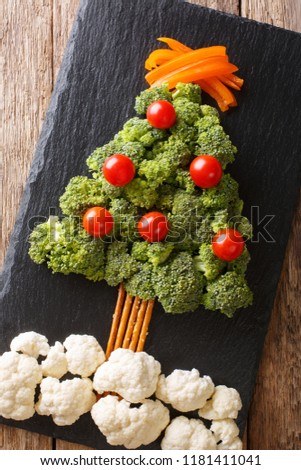 Festive food: a healthy Christmas tree of fresh broccoli, cauliflower, tomatoes, pepper closeup on a table. Vertical top view from above

