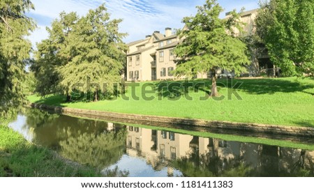 Panorama view mirror reflection of typical riverside apartment building complex in Irving, Texas, USA. Urban eco living place with a lot of mature trees and canal