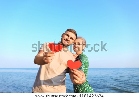Cute young couple with red hearts on sea shore