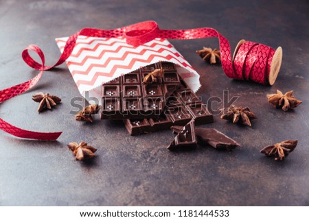 Set of sweet milk, white and dark chocolate bars in a red paper gift package, star anise on a metal rustic tray. Copy space for your text