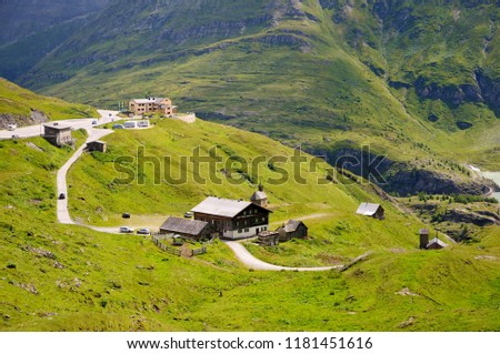 Several small houses and hotel buildings. Cars parked near buildings. Beautiful curving mountain road, Grossglockner Hochalpenstrasse, Austria. Summer day.