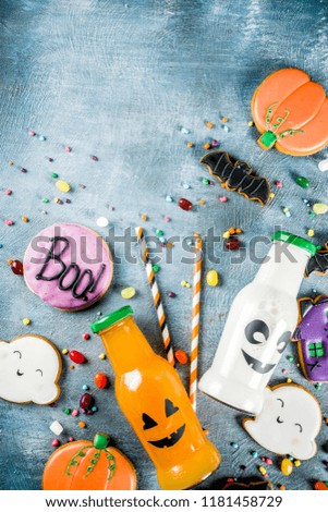 Kids treats for Halloween, funny homemade glazed cookies, various candies milk and juice in monster bottle, blue concrete background copy space top view