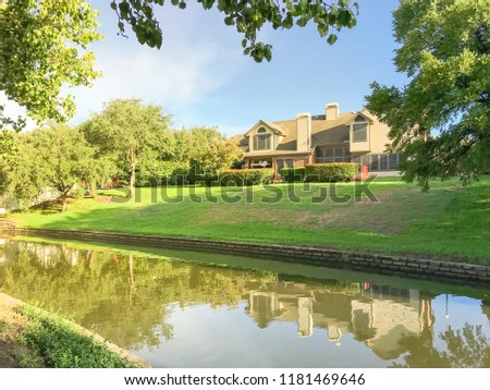 Mirror reflection of typical riverside houses surrounded by mature trees in Irving, Texas, USA.