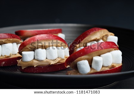 Fun food for kids. Halloween apple mouths filled with peanut butter with mini marshmallows for teeth. Shallow depth of field with selective focus on center treat. 