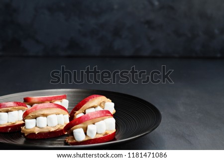 Fun food for kids. Halloween apple mouths filled with peanut butter with mini marshmallows for teeth. Shallow depth of field with selective focus on lips in the center of plate.  Free space for text.