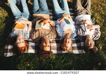 Top view of group of multhiethnic students laying on a grass with eyes closed, holding books