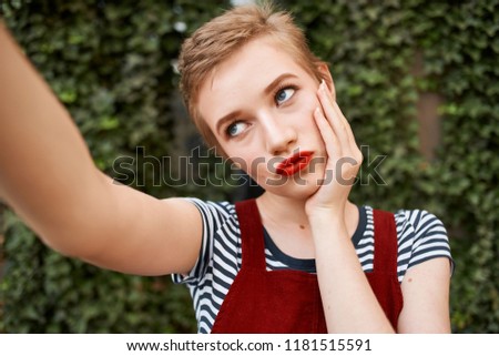 a woman with red lips takes pictures of herself against the background of bushes                               