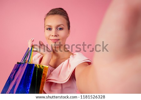 beautiful smiling blonde woman shopaholic bag photographing selfie on the phone pink background in studio . concept of seasonal black friday sale and online shopping