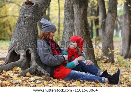 Young beautiful mother with her daughter on nature. A girl in a hat walks in park. Girl in autumn city park in leaf fall.

