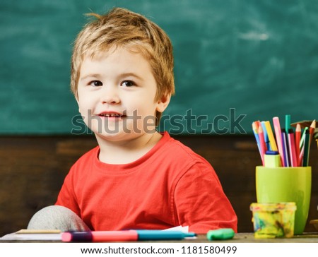 Little boy at art lesson. Smiling blond boy sitting at the desk with his knee bent.