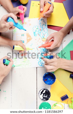 Markers in male and female hands draw house and rain on white paper. Artists wooden table with paints and colored paper. Hands hold colorful markers and draw. Art and artwork concept