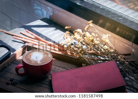 Latte cup,coffee bean,book and dried flowers jar on wooden tray with warm morning light near the window.Copy space.