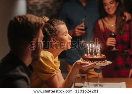 Beautiful young woman blowing candles on birthday cake.