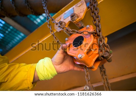 Industrial rigger rope access inspector worker hand commencing safety daily inspection on lifting hoist chain block prior to use on construction site 