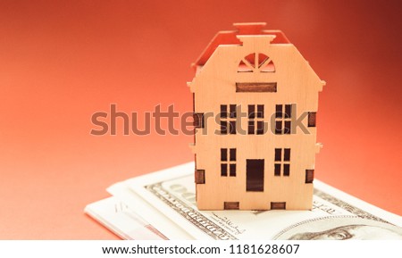 pale picture yellow wooden model house on a pile with money on a red background with copy space.